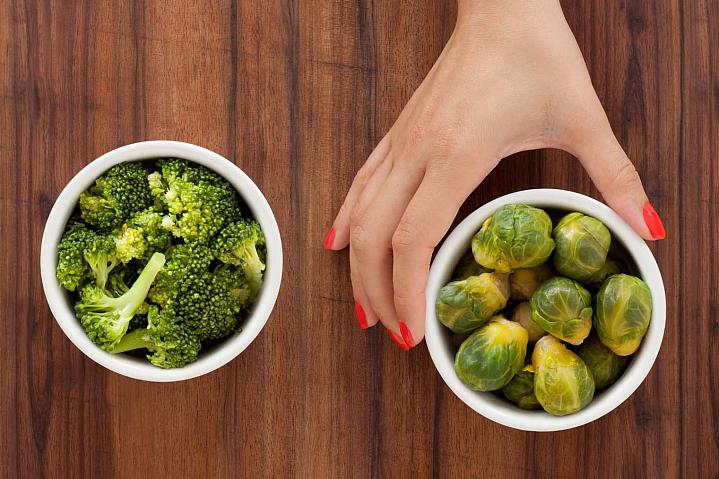 Person's hand choosing brussel sprouts over broccoli cropped