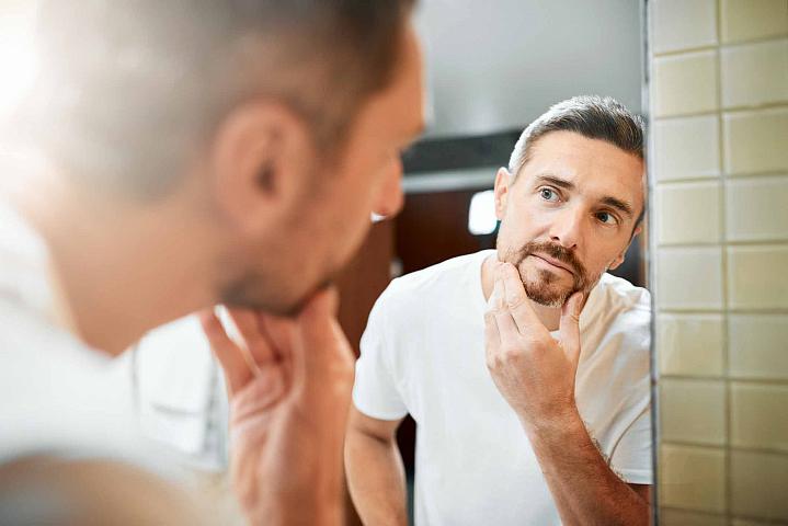 Man looking in the mirror at the gray hair in his beard Man looking in the mirror at the gray hair in his beard