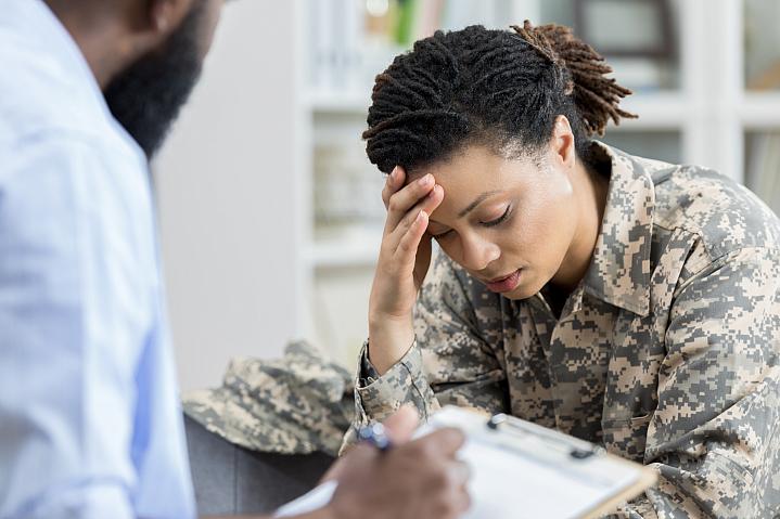 Female military veteran holding her head in an appointment with a health care professional