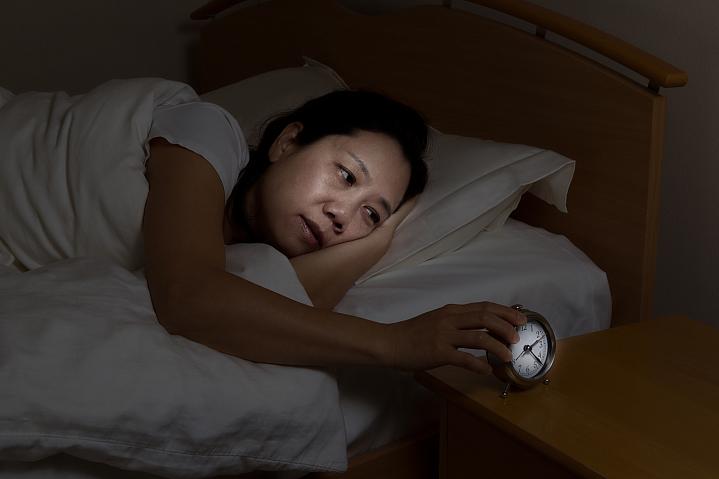 Woman awake in bed touching the alarm clock