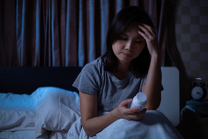 Woman sitting up in bed reading a pill bottle Woman sitting up in bed reading a pill bottle