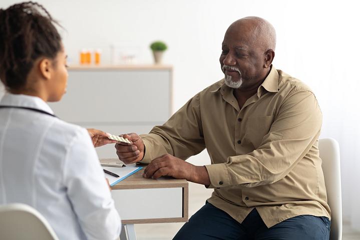 Health care provider handing older adult patient a pack of pills